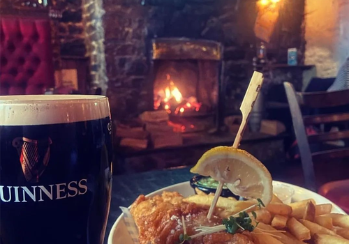 a pint of guinness and fish and chips in a pub, with an open fire in the background