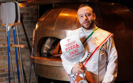 man holding award in front of a pizza oven
