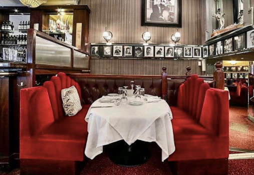 interior of trocadero restaurant. Table covered with white tablecloth, red velvet seats on either side. Black and white pictures of celebrities hanging on wall in background