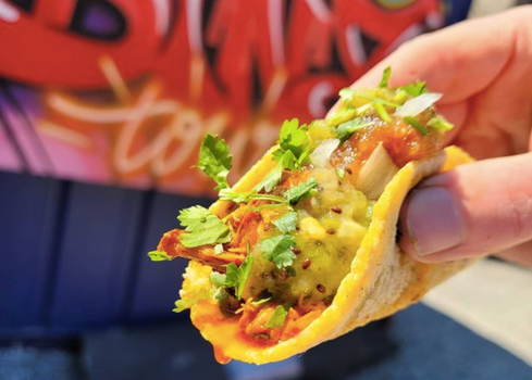 close up of a taco loaded with cheese, meat and coriander. Street art in background