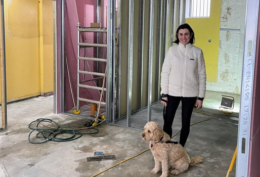 Woman and a dog standing in a restaurant in the process of being refurbished - exposed floors, ladders in the background, building equipment etc