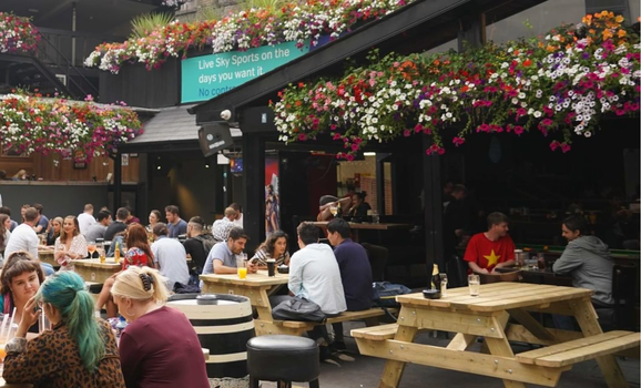 outdoor beer garden with hanging flower baskets and people sitting on picnic benches