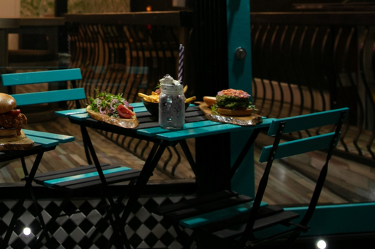 table and chairs outside a restaurant, on the table is an assortment of burgers, loaded fries and milkshakes