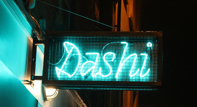 Neon blue sign which reads "Dashi", outside a cocktail bar