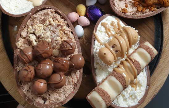 Two halves of an Easter egg filled with cheesecake and chocolate toppings including malteasers and kinder bueno.