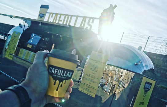 coffee cup held up outside cafollas food truck with sun shining in the background