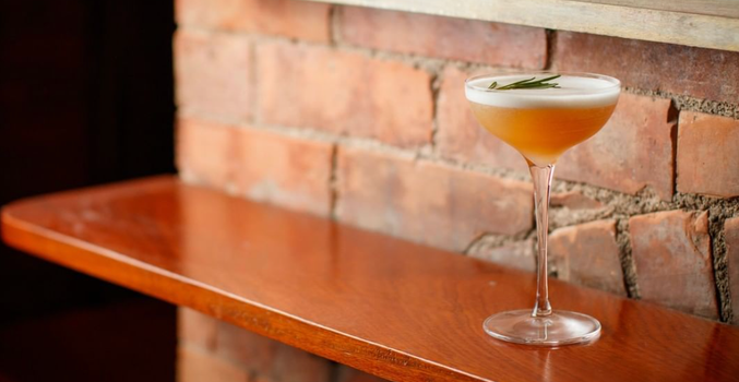 cocktail in a tall glass on a wooden ledge with red brick wall in the background