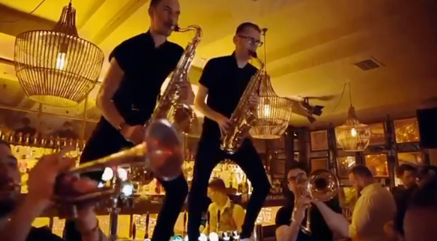 two trumpeteers playing on top of a bar in a busy nightclub