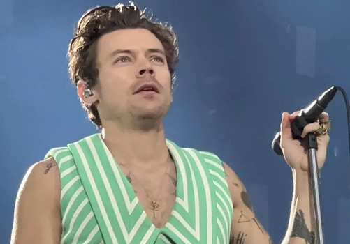 harry styles in green and white pinstriped sleeveless suit, holding a microphone and mic stand