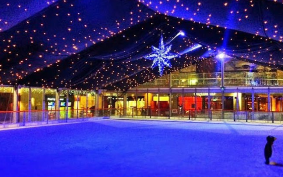 empty iceskating rink at nighttime with a fabric ceiling and fairy lights overhead.