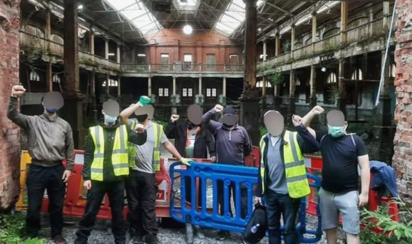 group of people with faces blurred out, some in hi vis vests, standing in front of the iveagh markets