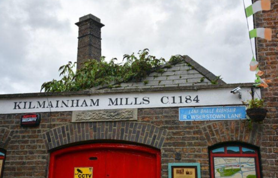 old brick building with red door and industrial style tower in background, with a sign that reads Kilmainham Mills C1184