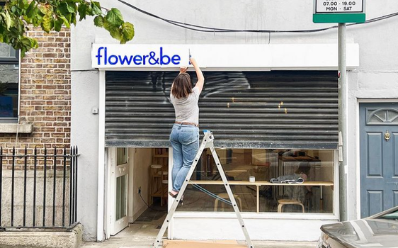 woman on step ladder painting the sign on a shop front