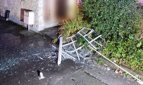 the smashed remains of a window in the front garden of a home after a house fire