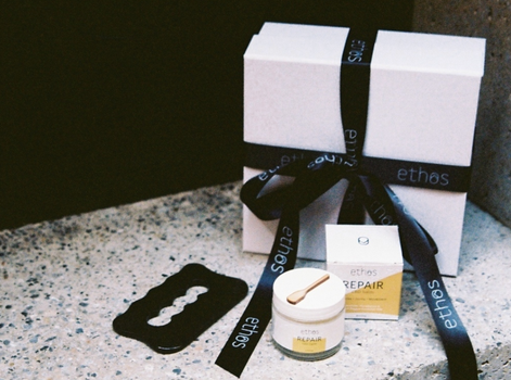 white gift box with black ribbon and small tubs and pots in front of it