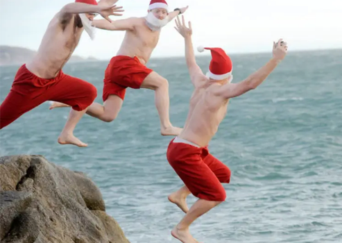 three men wearing santa hats and beards jumping off a rock into the sea