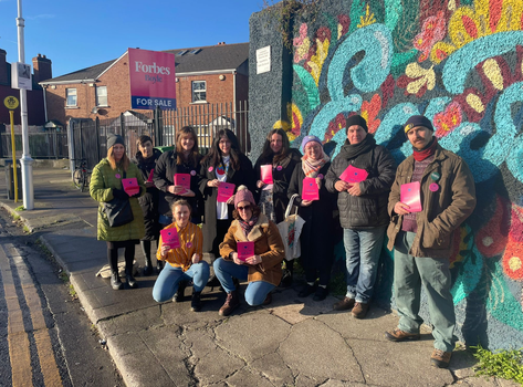 group of fundraisers on a street corner in east wall, all holding bright pink leaflets