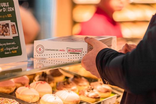 a person being handed a box of krispy kreme donuts over the glass counter, under which more donuts can be seen