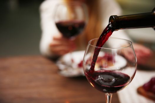 red wine being poured into a glass, a person out of focus in the background holding a second glass