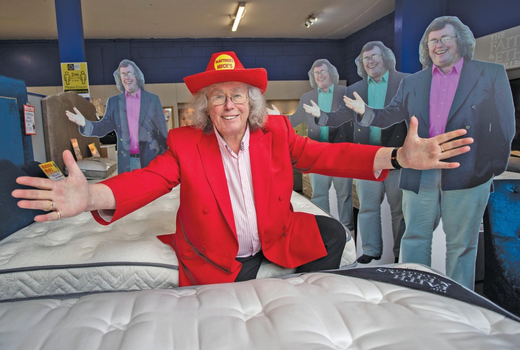 mattress mick posing in a red suit and hat at his mattress shop